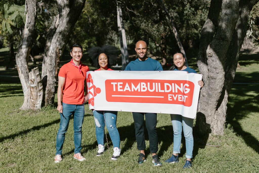 Über uns Group of four diverse adults holding a team building banner in a sunny park.